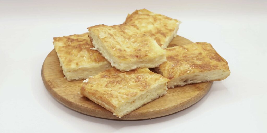 Domaća gibanica sa sirom, hrskava i bogato filovana, servirana na drvenom tanjiru.