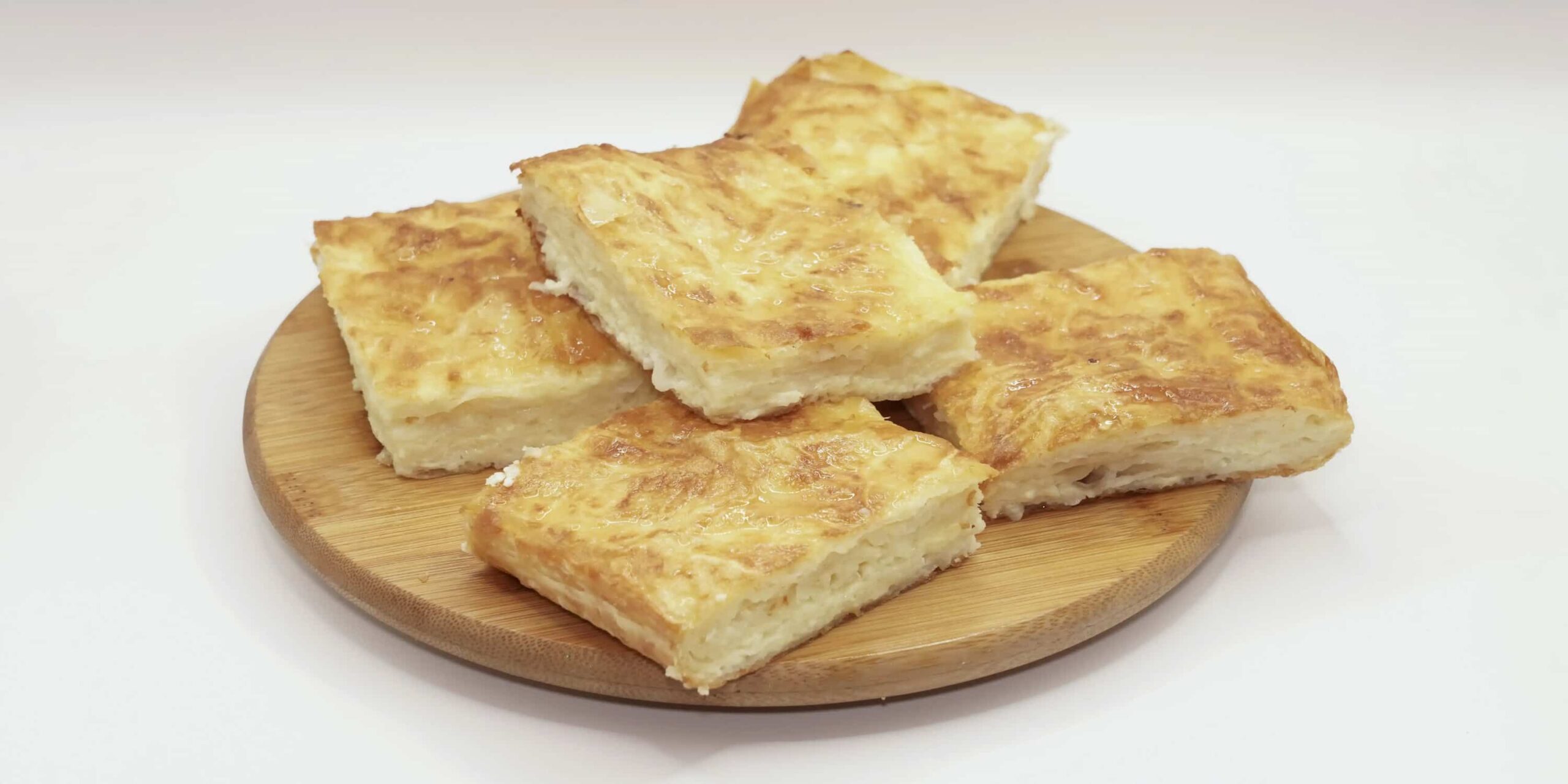 Domaća gibanica sa sirom, hrskava i bogato filovana, servirana na drvenom tanjiru.